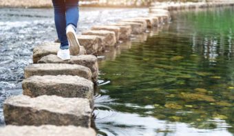 Trittstein_Überbrückung Frau geht über Trittsteine im Wasser